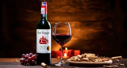 Bon Voyage red wine bottle with a glass of red wine, grapes and corks on a rustic table